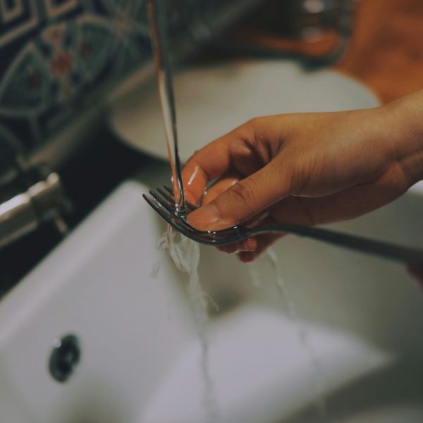 Photo of a person washing a fork in the kitchen sink.