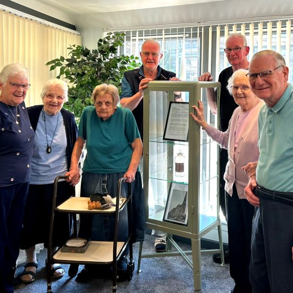 Photo of tenants standing by a display case holding the bottle.