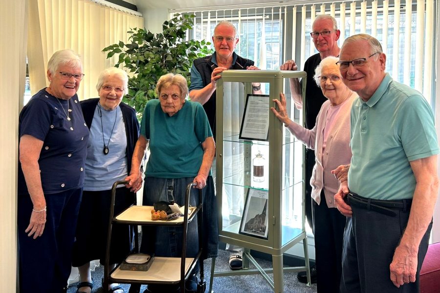 Photo of tenants standing by a display case holding the bottle.