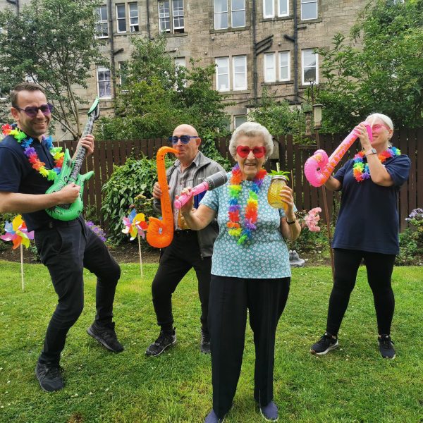 Photo of staff and tenants dancing in a garden with inflatable instruments.