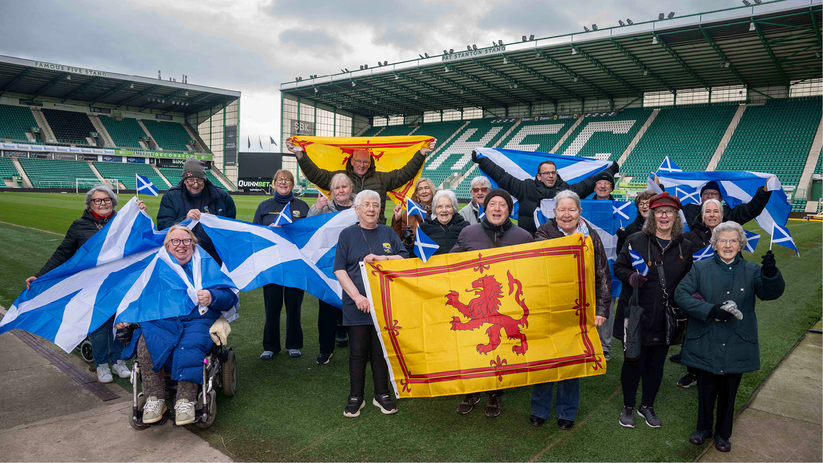 Photo of a group of sheltered housing tenants waving large Scotland flags inside Easter Road Stadium.