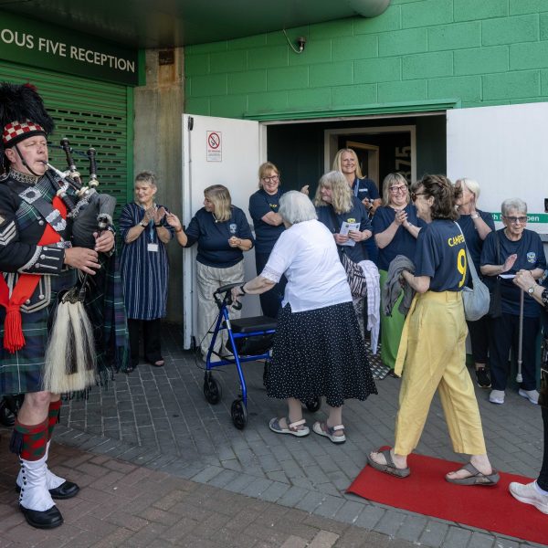 Photo of Leith Legends walking the red carpet beside a bagpiper at Easter Road Stadium.