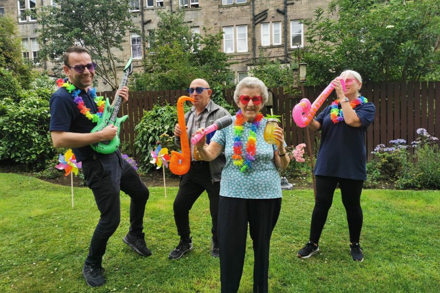 Photo of staff and tenants dancing in a garden with inflatable instruments.