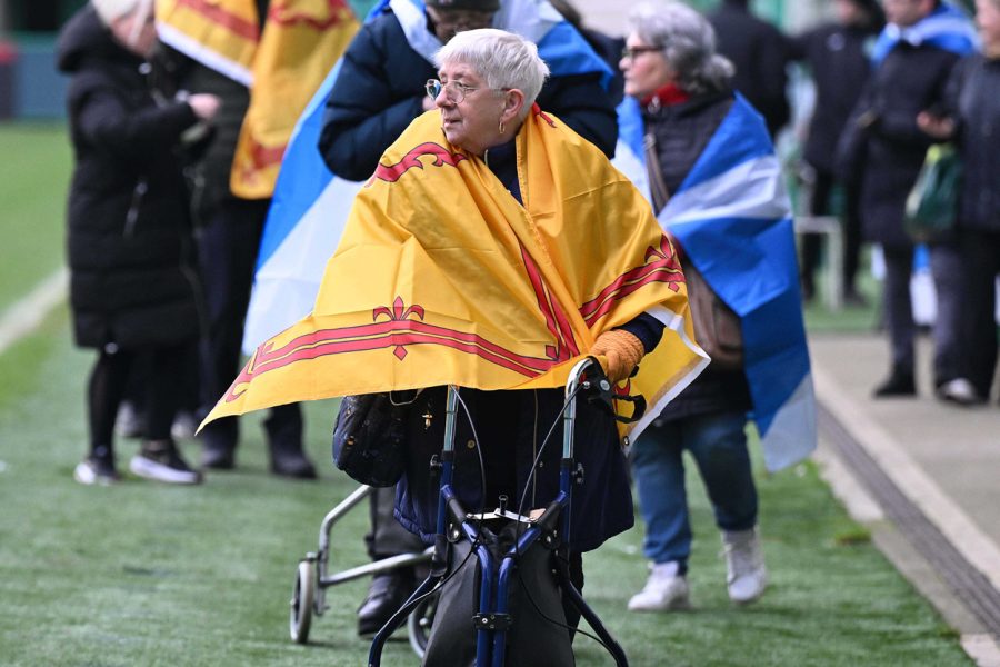 Photo of woman walking with a royal banner of Scotland flag on tied round her shoulders.