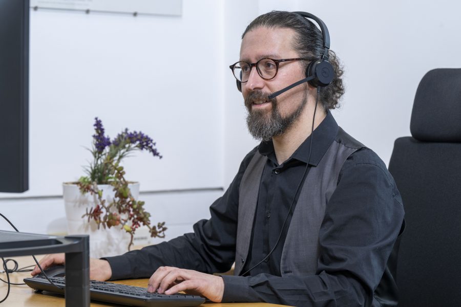 Photo of a man wearing a headset and sitting at a computer.