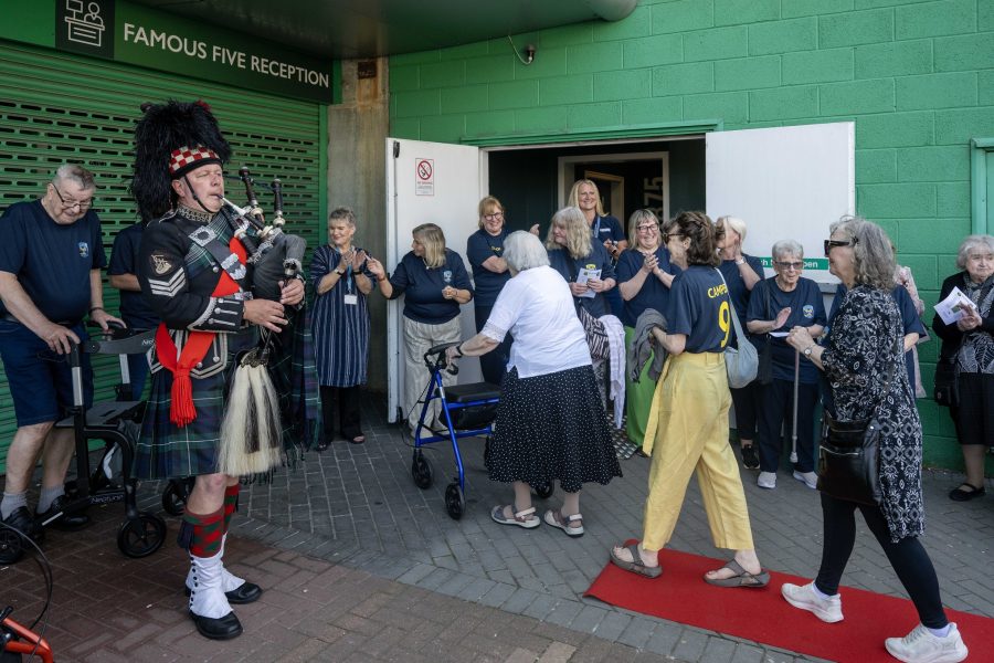 Photo of Leith Legends walking the red carpet beside a bagpiper at Easter Road Stadium.